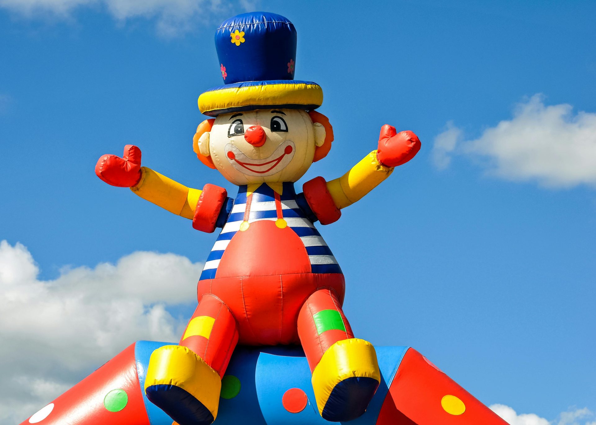Ein farbenfroher, aufblasbarer Clown auf einem Jahrmarkt unter einem strahlend blauen Himmel, der Spaß und Freude symbolisiert.